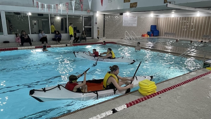 Jeunes enfants et adolescents sur un kayak dans une piscine en train de ramer.