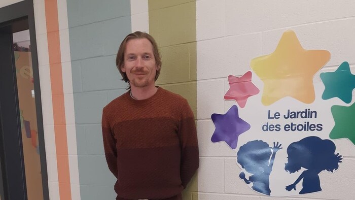 Yoan Rousseau pose pour la photo à côté d'une affiche du centre de la petite enfance Le Jardin des étoiles.