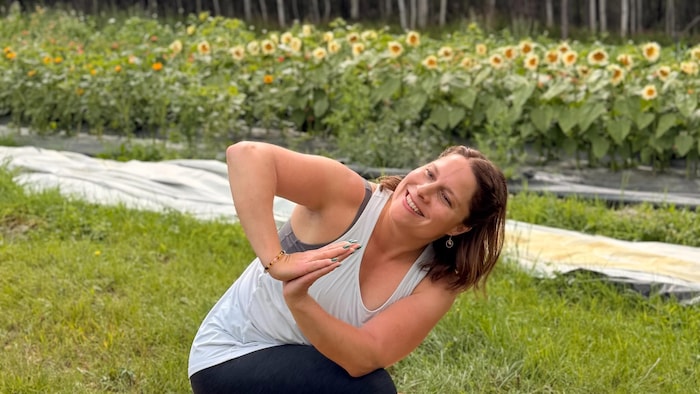 Joannie Jacob en position de yoga et souriante sur un tapis sur la ferme des Pelures.