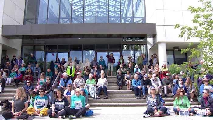 Des dizaines de personnes sont assises dehors devant un édifice avec des affiches au cou.