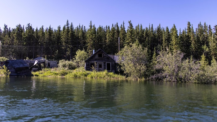 Une vieille maison de bois devant une grande étendue d'eau.