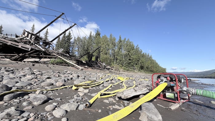 Une pompe à eau et des tuyaux près d'une épave, sur une berge. 