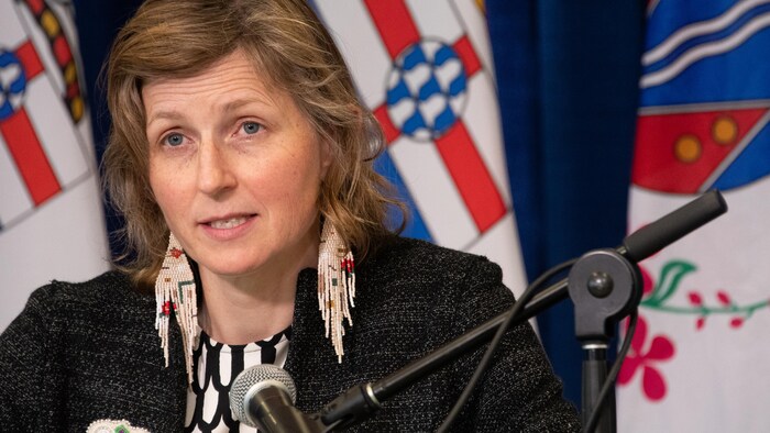 La médecin hygiéniste en chef intérimaire Catherine Elliott parle dans un micro devant des drapeaux.