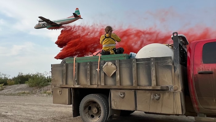 Un avion disperse de la poudre antifeu, au premier plan, un camion avec une personne en uniforme de pompier, en juillet 2023.