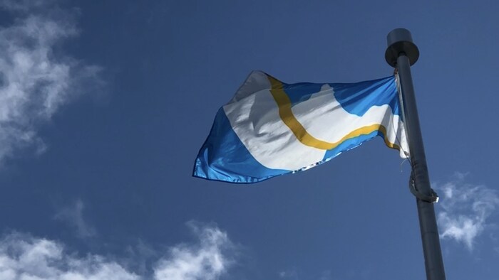 Le drapeau franco-yukonnais flotte au vent sur fond de ciel bleu.
