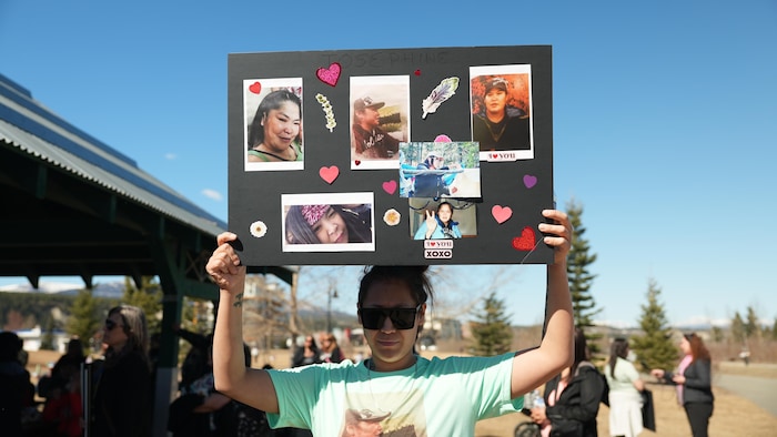 Une femme tient une pancarte décorée des photos d'un homme et d'une femme, le 26 avril 2024.