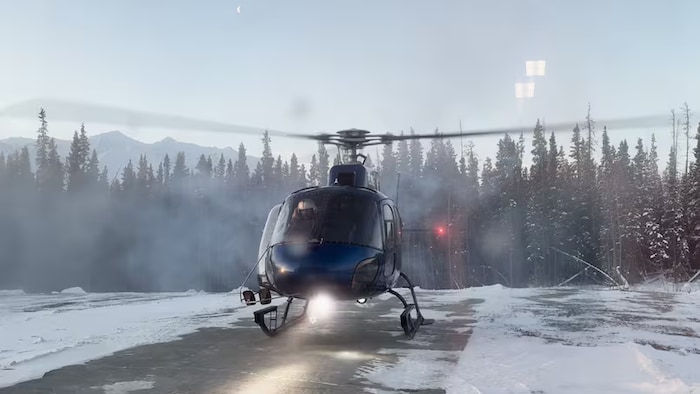 Un hélicoptère s'apprête à décoller avec une forêt en arrière-plan.