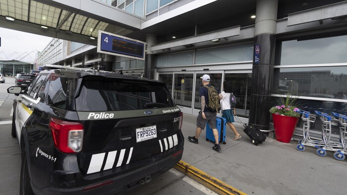 Des voyageurs passent devant une voiture de police de la Sûreté du Québec à l'aéroport international Montréal-Trudeau.