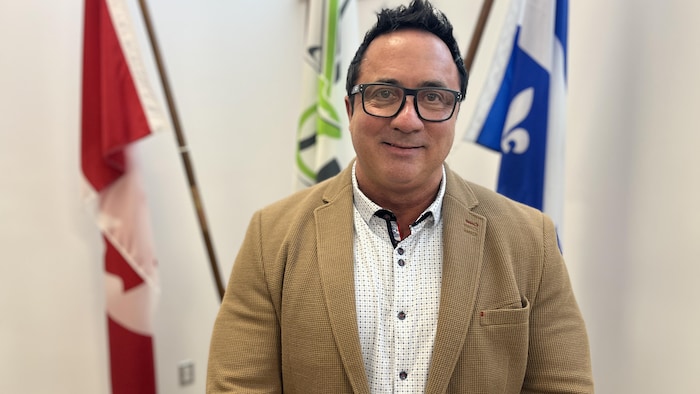 Yves Dubé pose près d'un drapeau du Canada, de la Ville de La Sarre et un drapeau du Québec.
