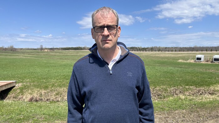 Yves Laurencelle pose aux abords d'un champ verdoyant. Il est ne sourit pas et regarde directement la caméra. 