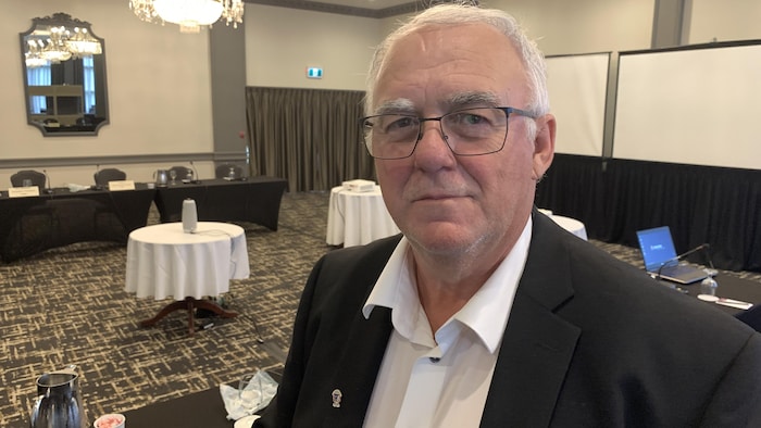 Yvon Godin pose pour une photo dans une salle de conférence, sous un chandelier. 