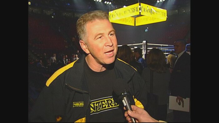 Un homme en entrevue à Radio-Canada devant un ring de boxe.