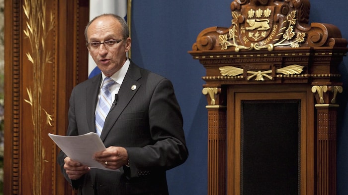 Yvon Vallières, debout devant le siège du président de l'Assemblée.