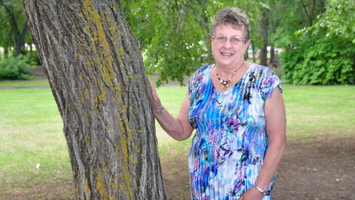 Yvonne Bisson sourit à la caméra, sa main posée sur un tronc d'arbre.