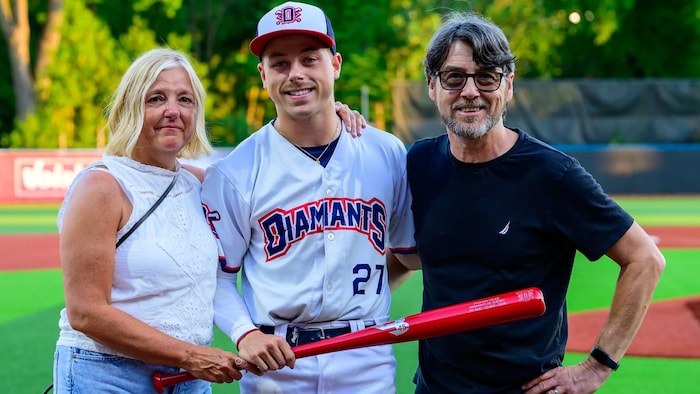 Il pose avec un bâton rouge dans les mains entouré de ses parents. 