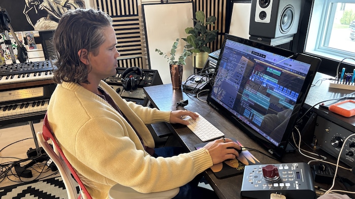 L'artiste est assis à l'ordinateur devant une session de montage musical.