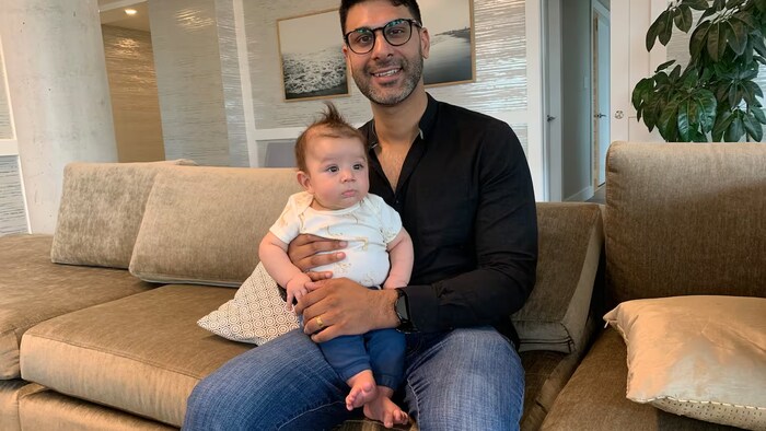 Zahir Shivji tient son bébé dans ses mains, sur un divan.