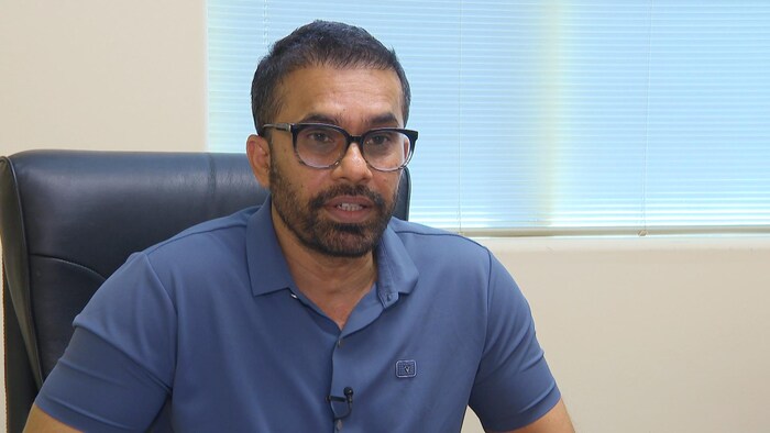 Un homme vêtu d'un polo bleu assis sur une chaise de bureau en cuir.