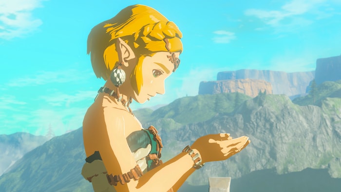 Un personnage de jeu vidéo regarde ses mains, devant un paysage rocailleux. 