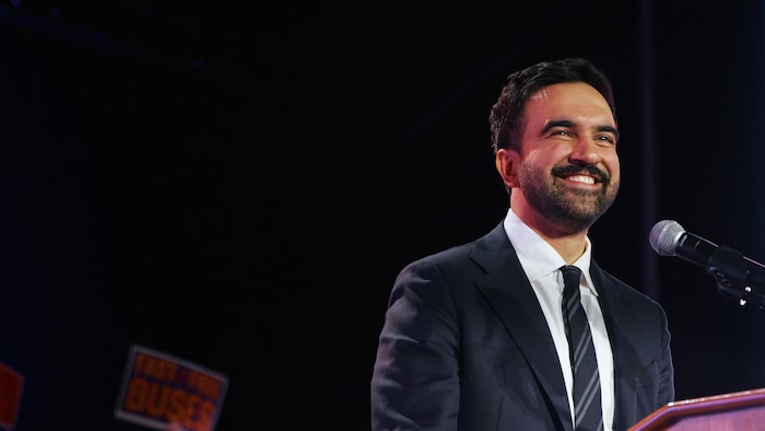 Derrière un lutrin, Zohran Mamdani sourit à la foule.