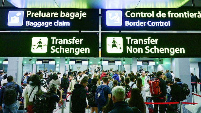 Des voyageurs marchent dans un aéroport à proximité de panneaux qui indiquent les zones Schengen et non Schengen.
