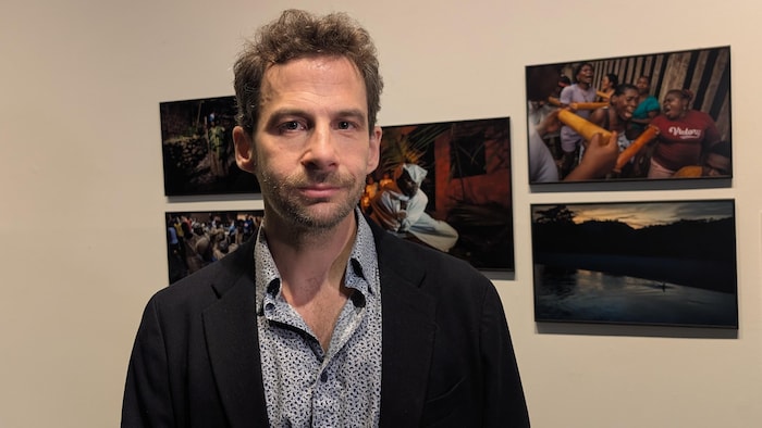 Un homme pose devant des photos sur un mur.