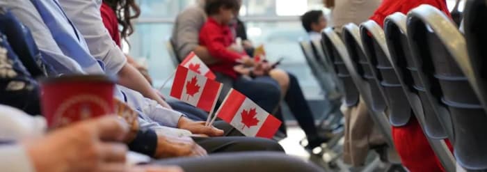 Personas con pequeñas banderas canadienses sentadas en una sala esperando la ceremonia de ciudadanía.