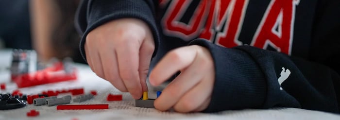 Un enfant joue aux legos. Gros plan sur ses mains.