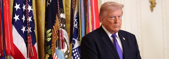 Donald Trump debout devant des drapeaux.