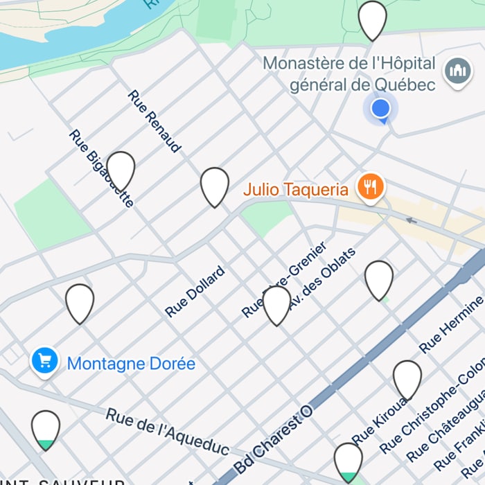 Capture d'écran de l'application mobile "à vélo" affichant une carte stylisée de la ville de Québec. Plusieurs marqueurs de localisation blancs en forme de goutte et un cercle bleu, représentant probablement des stations de vélos, sont dispersés sur la carte.