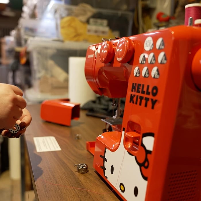 Une personne en train d'entourer du fils sur une bobine à côté d'une machine à coudre. 