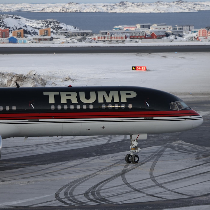 Un avion sur lequel est écrit « Trump » est posé devant un paysage de neige et de maisons.