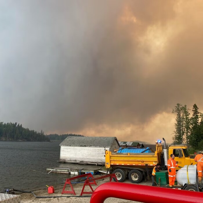 Des travailleurs qui font le plein d'eau près d'une rivière sous un ciel rempli de fumée.