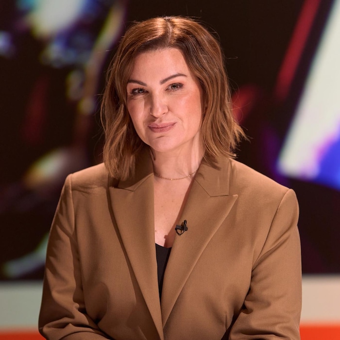 Une femme portant une veste brune sourit. 