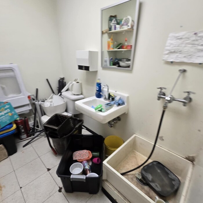 Une salle de toilette avec un seau de vadrouille à l'intérieur, ainsi que des bacs pêle-mêle.