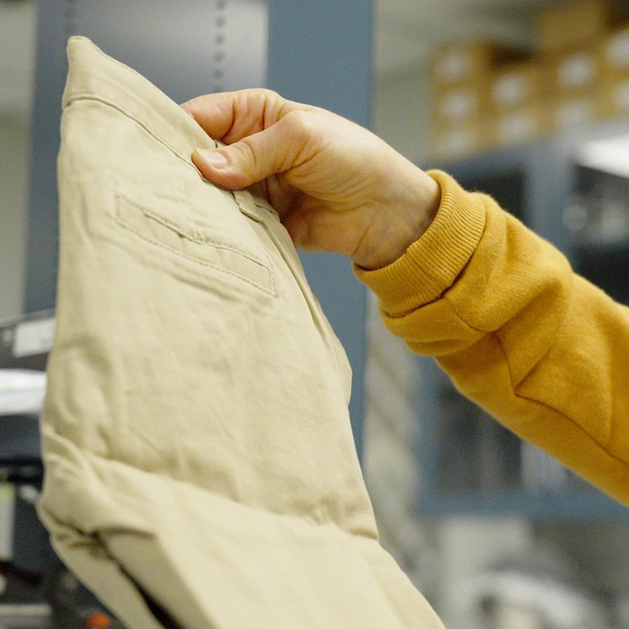 Une main tient un petit pantalon pour enfant. La scène a lieu dans un laboratoire.