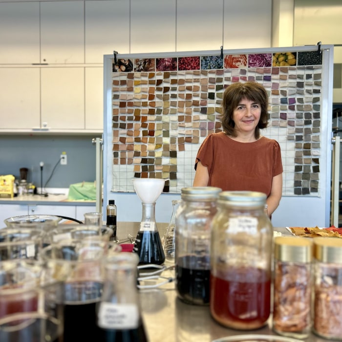 Une femme se tient debout derrière des bocaux remplis de teintures colorées dans un laboratoire.