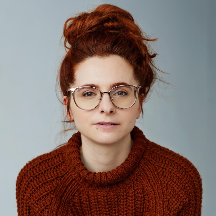 Une femme rousse portant des lunettes regarde l'objectif.