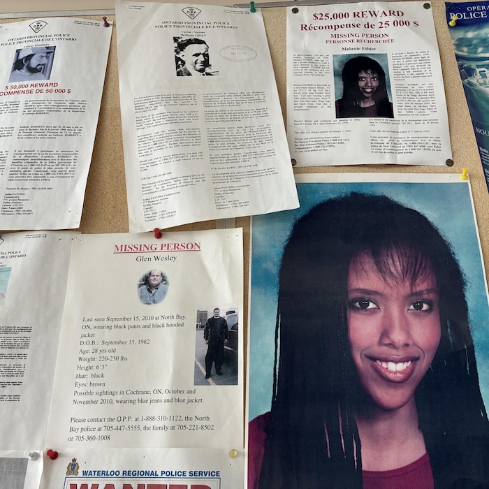 Un babillard avec plusieurs affiches de gens disparus. On y trouve la photo de Mélanie.
