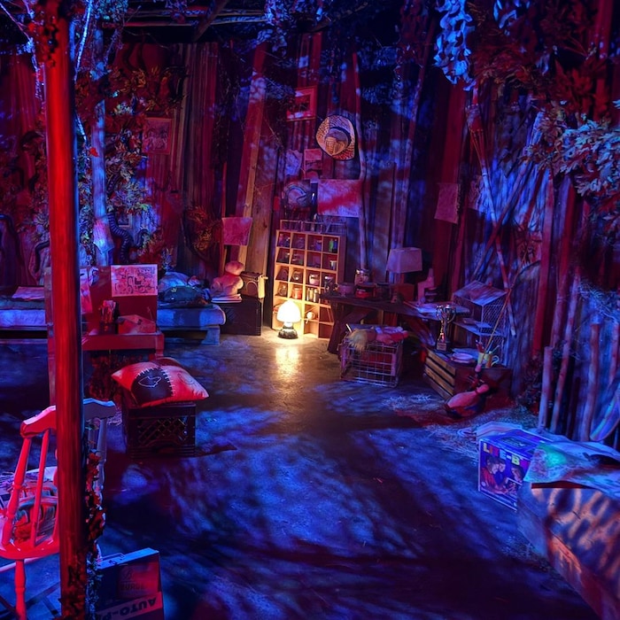 Une pièce sombre est décorée avec de faux arbres, une vieille chaise et une lampe.