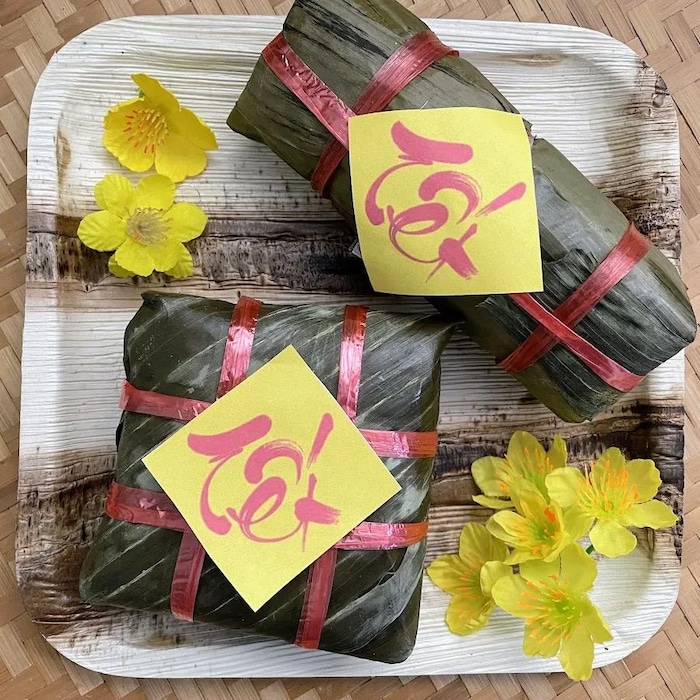 Des gâteaux sont enveloppés étroitement dans des feuilles de bananiers. Des écritures indiquent « Têt » sur chaque gâteau. 