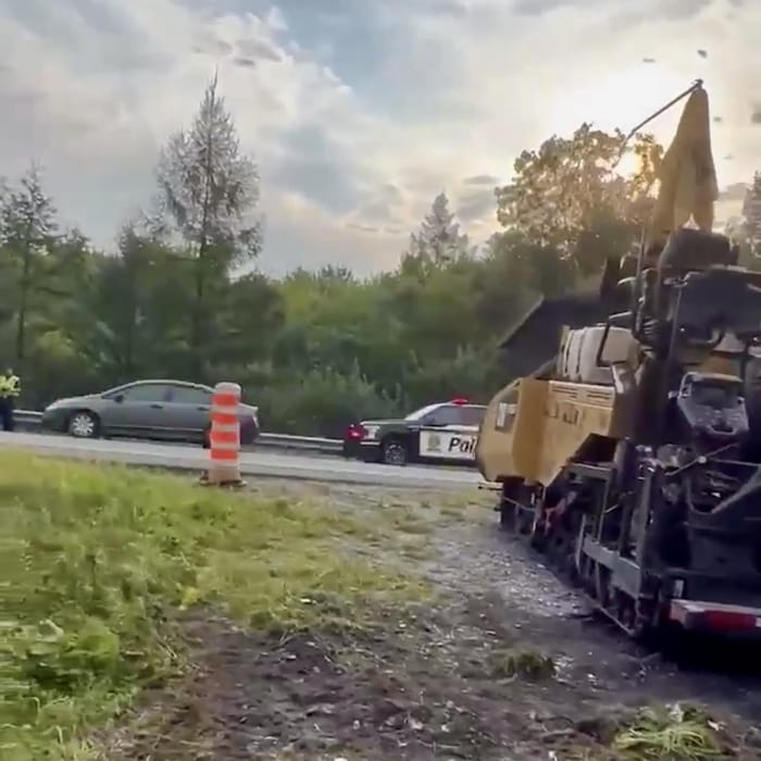 Terre-plein centrale d'une autoroute avec une paveuse et une voiture de police.