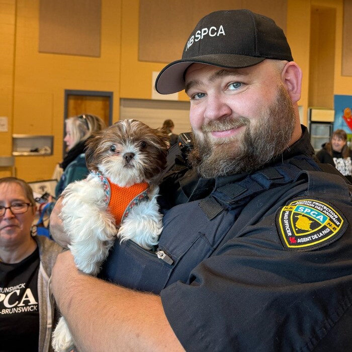 Un agent en uniforme tenant un chien dans ses bras sourit à la caméra.