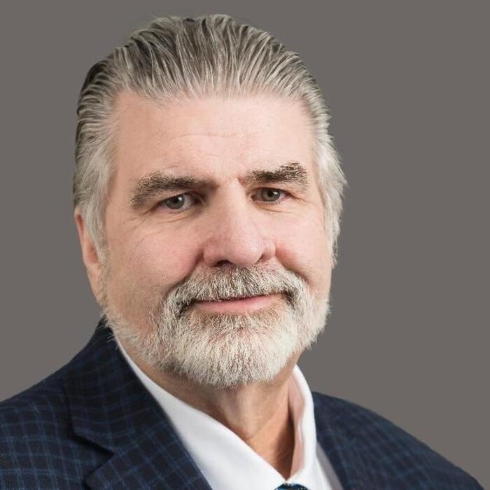 Portrait professionnel d'un homme à la barbe grisonnante et aux cheveux bien coiffés.