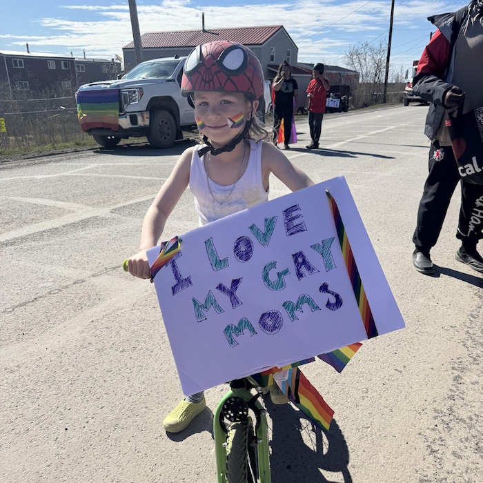 Une enfant à vélo dans une parade tient une affiche sur laquelle est inscrit « J'aime mes deux mamans gaies ». 
