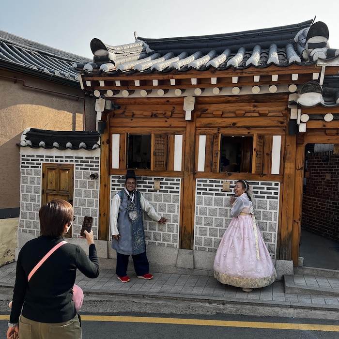 Deux personnes se font photographier devant une maison ancestrale. 