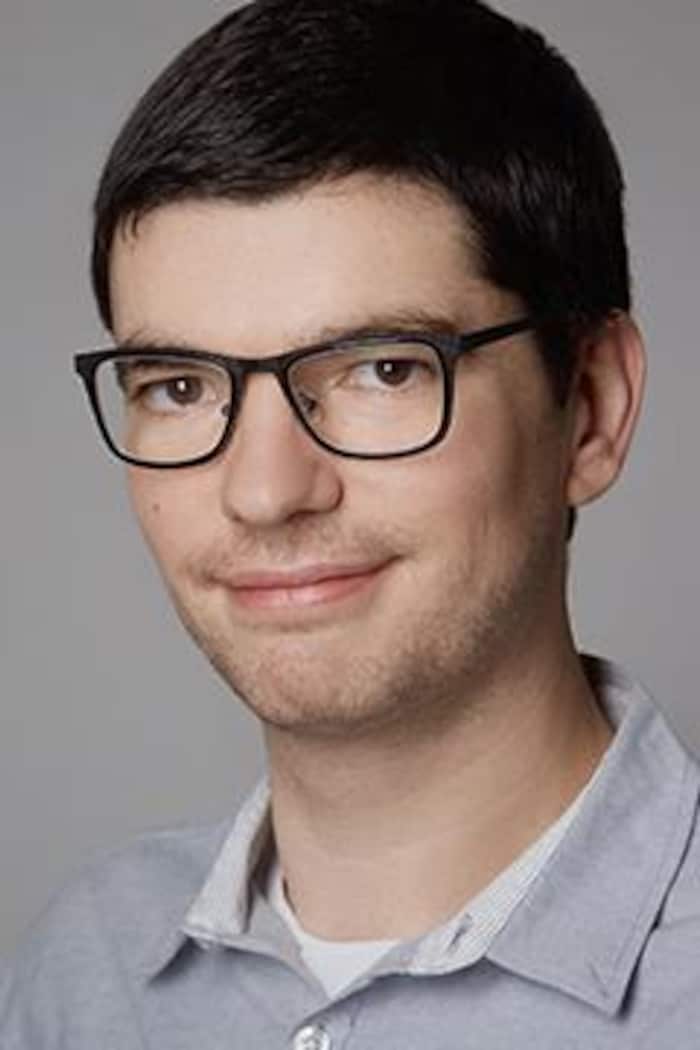 Un homme avec des lunettes prend la pose, légèrement souriant.