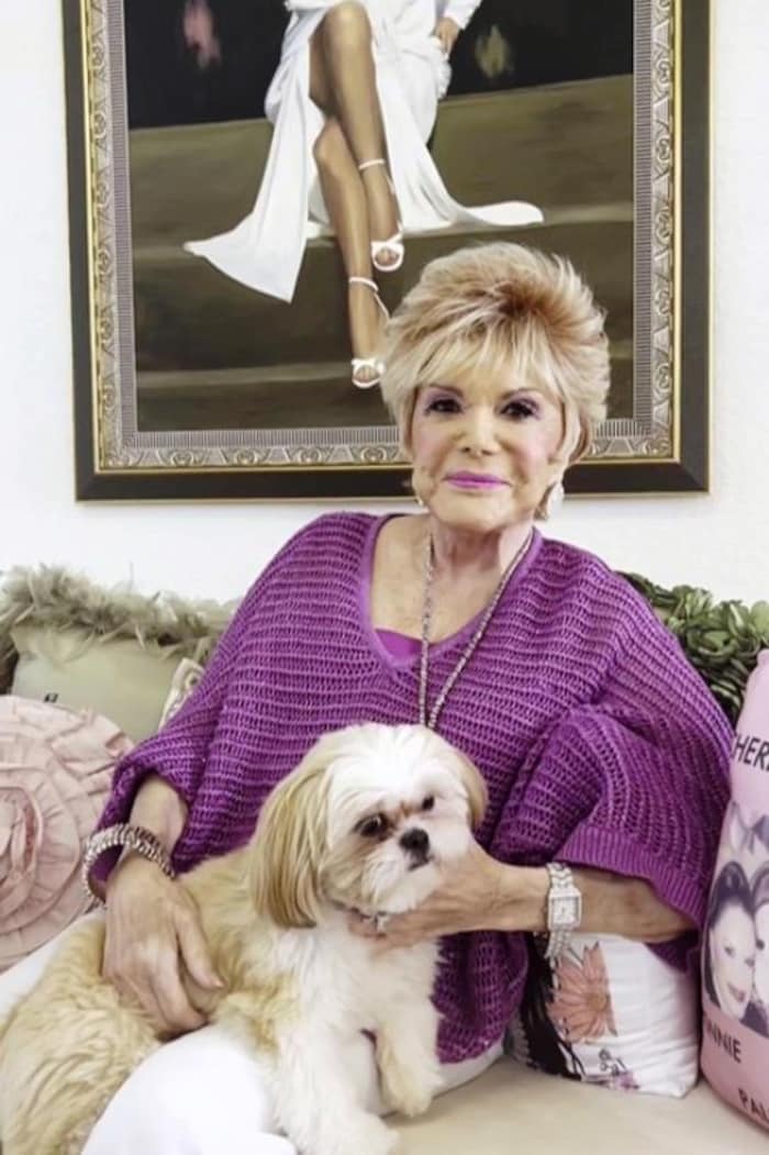 Une femme aux cheveux courts blonds pose avec un petit chien.