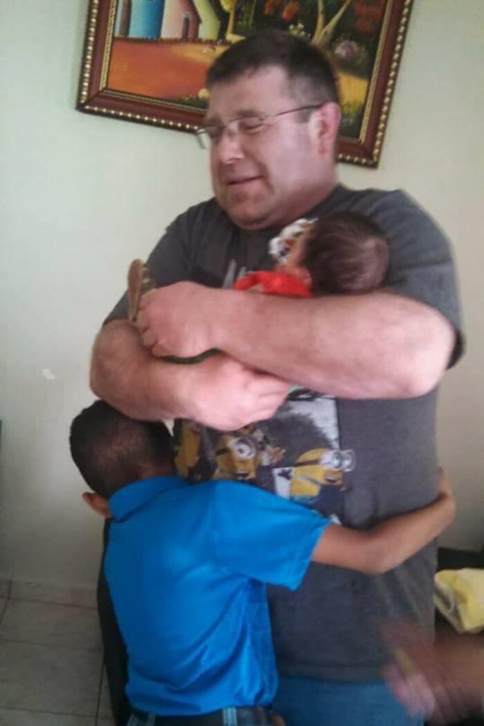 Danny tient un jeune bébé dans ses bras pendant qu'un petit garçon lui fait un câlin.