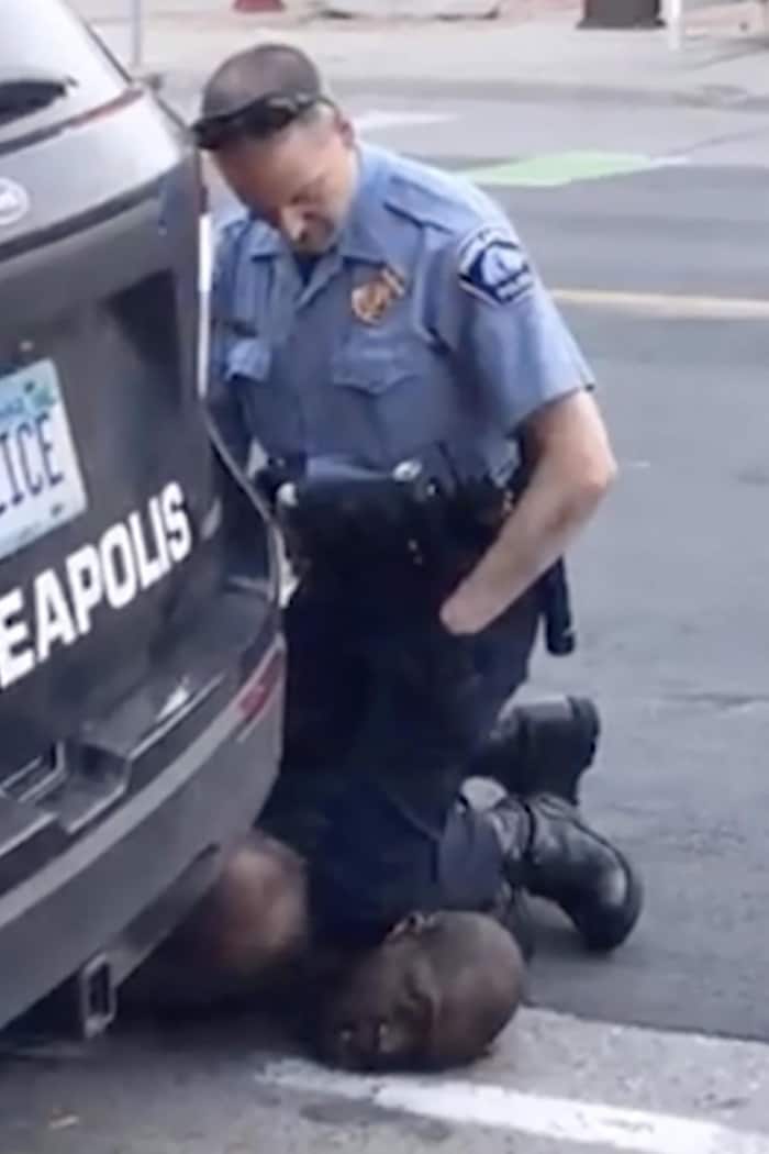 Un policier est accroupi à genoux sur le cou d'un homme noir, plaqué au sol, en pleine rue.